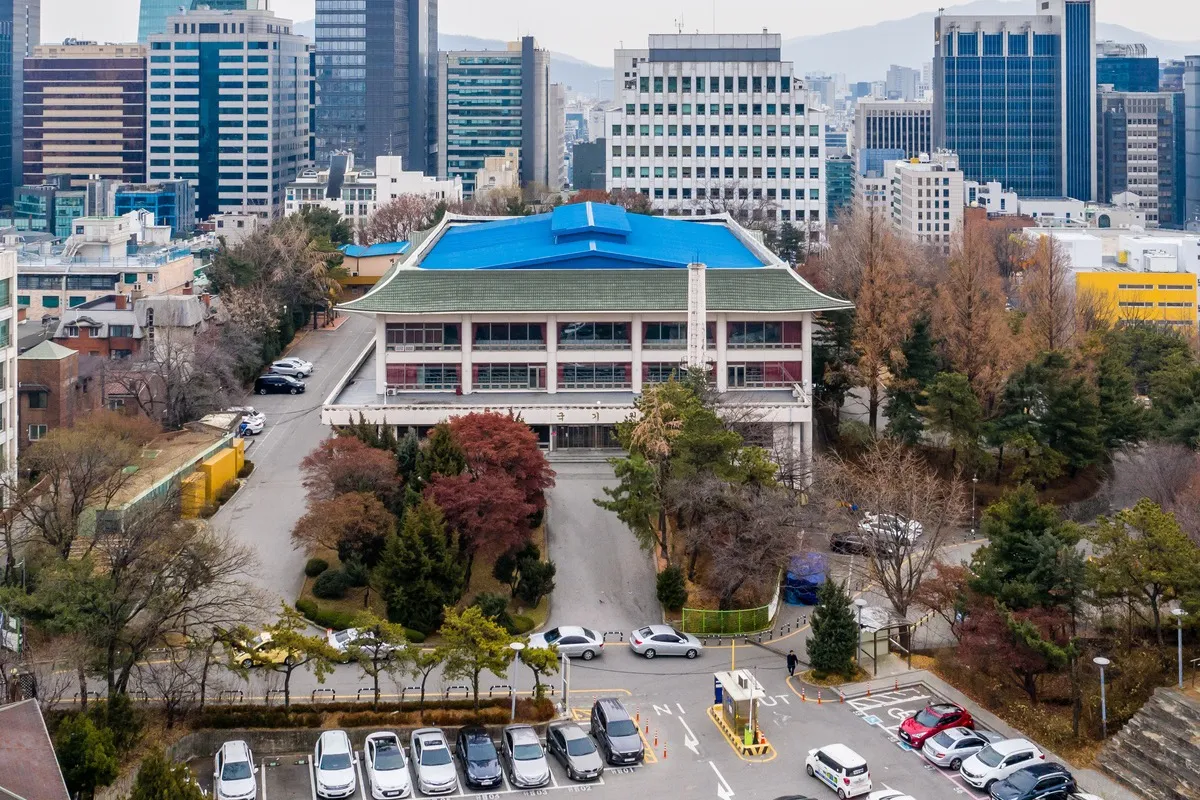Das Kukkiwon: ein Gebäude mit geschwungenem grünem Ziegeldach und blauem Dach, umgeben von Bäumen und Hochhäusern