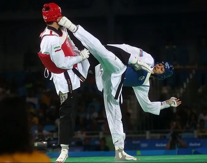 Zwei Taekwondo-Kämpfer mit Kopfschutz und Trefferwesten; einer trifft mit einem hohen Fußtritt den Kopfschutz des anderen